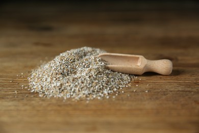 Photo of Pile of fresh rye bran and scoop on wooden table