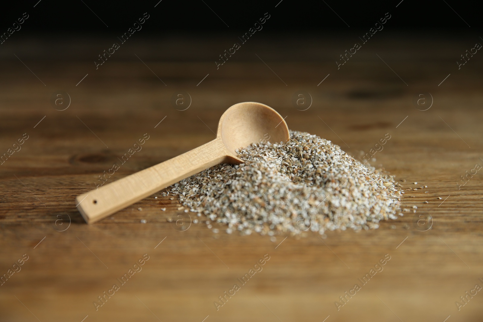 Photo of Pile of fresh rye bran and spoon on wooden table, closeup