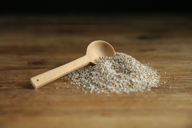 Photo of Pile of fresh rye bran and spoon on wooden table, closeup