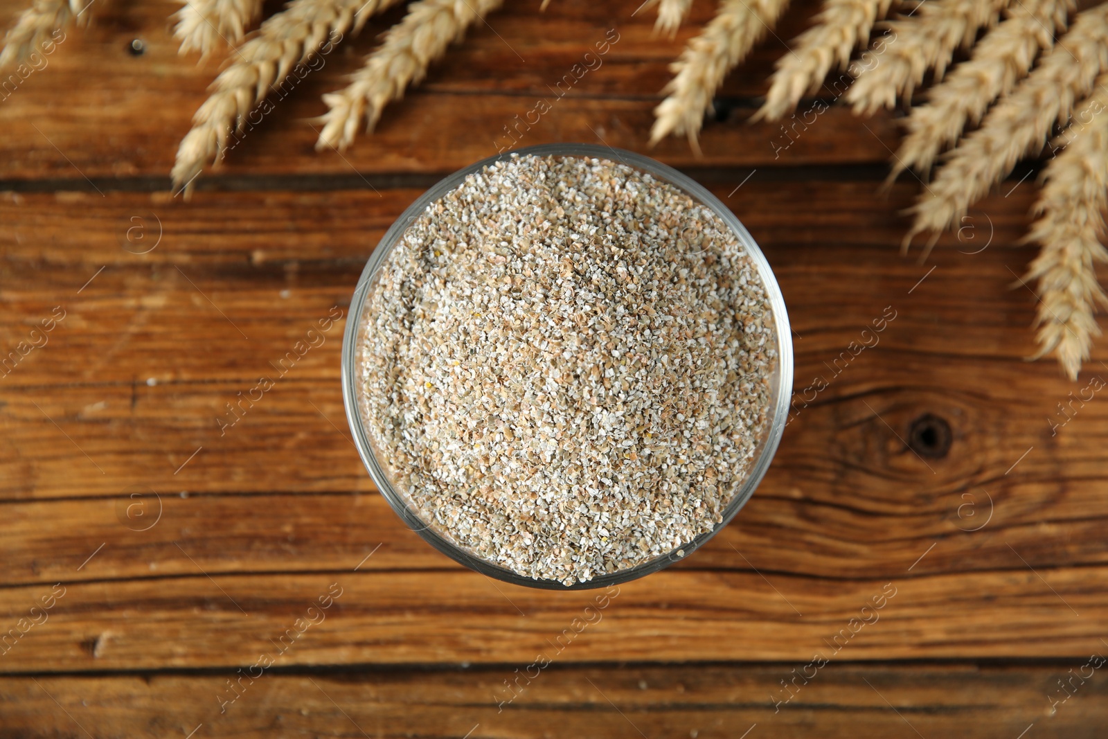 Photo of Fresh rye bran in bowl and spikelets on wooden table, flat lay