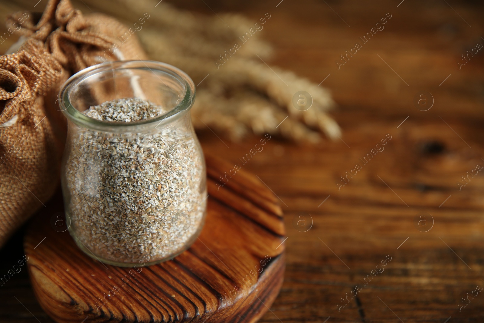 Photo of Fresh rye bran in jar on wooden table, closeup. Space for text