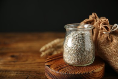 Photo of Fresh rye bran in jar and sack on wooden table, closeup. Space for text