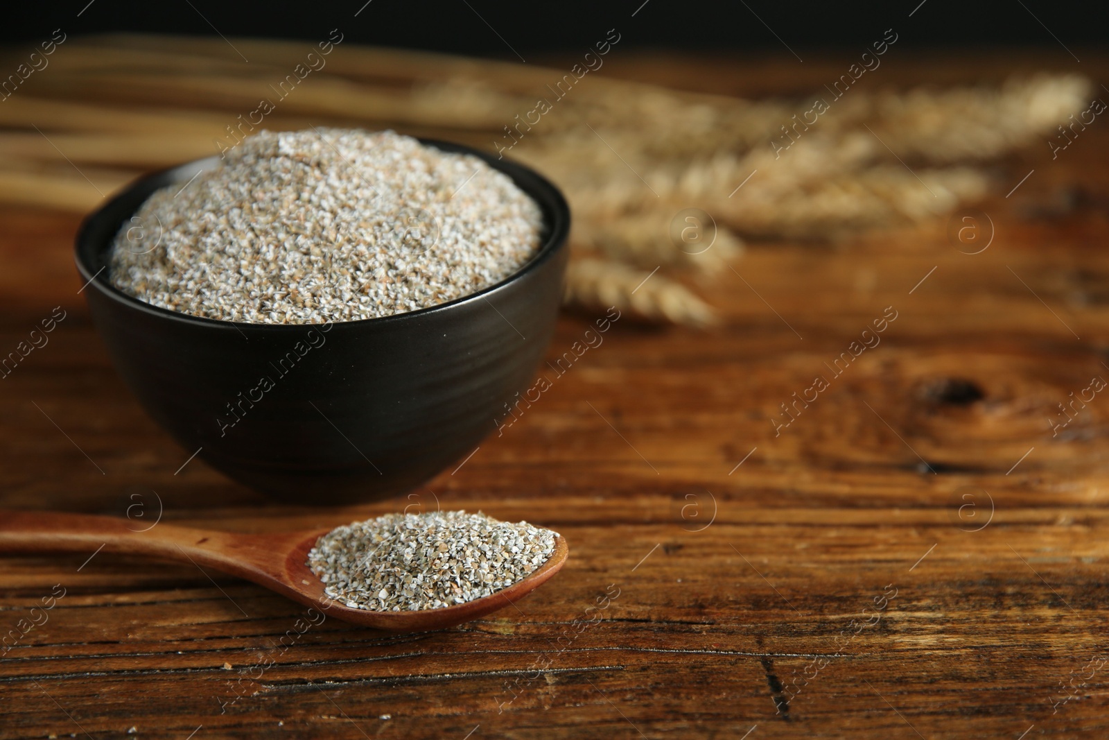 Photo of Fresh rye bran in bowl and spoon on wooden table, closeup. Space for text