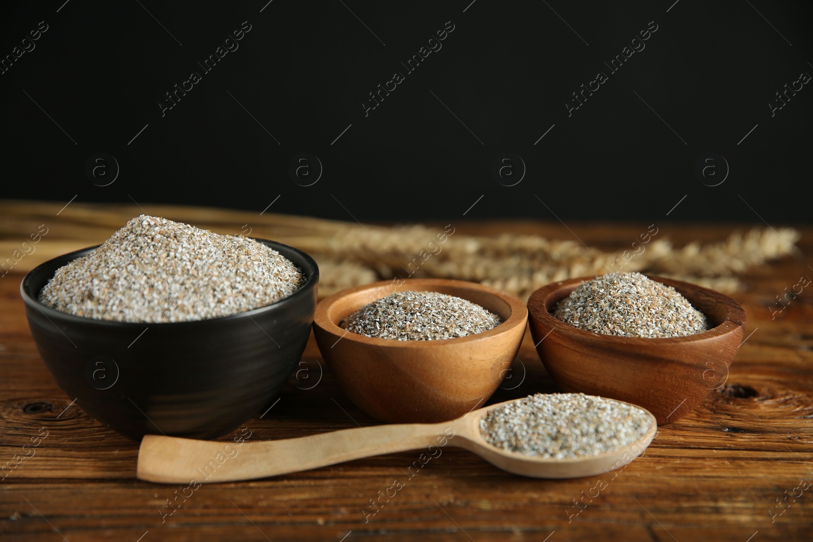 Photo of Fresh rye bran in bowls and spoon on wooden table, closeup