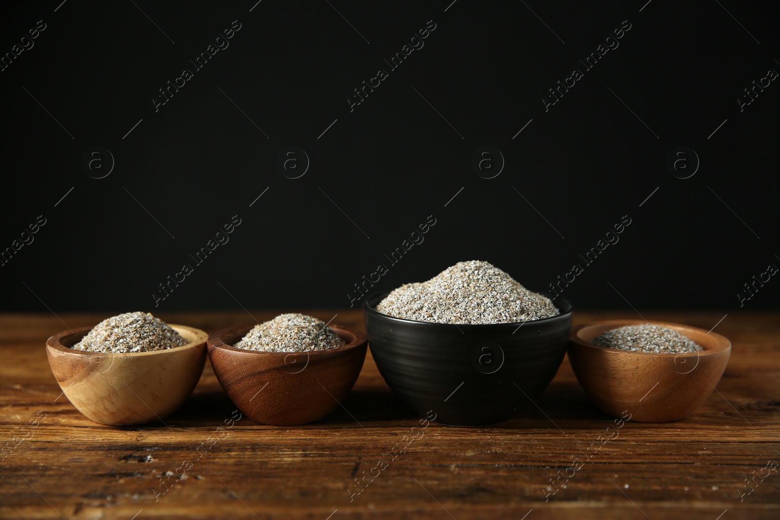 Photo of Fresh rye bran in bowls on wooden table against black background. Space for text