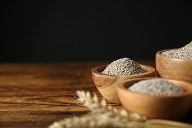 Photo of Fresh rye bran in bowls on wooden table against black background, closeup. Space for text