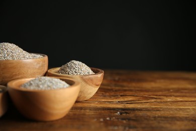 Photo of Fresh rye bran in bowls on wooden table against black background, closeup. Space for text