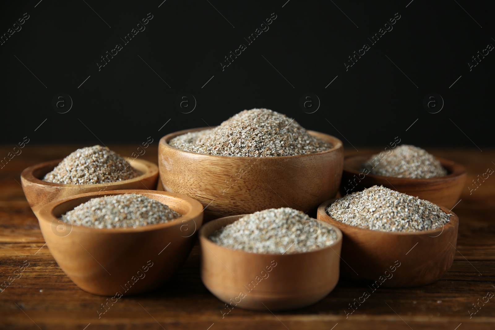 Photo of Fresh rye bran in bowls on wooden table against black background, closeup