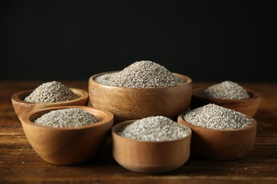 Photo of Fresh rye bran in bowls on wooden table against black background, closeup