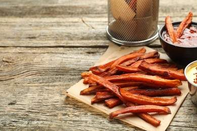 Delicious sweet potato fries with sauces on wooden table, closeup. Space for text