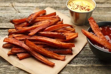 Photo of Delicious sweet potato fries with sauces on wooden table, closeup