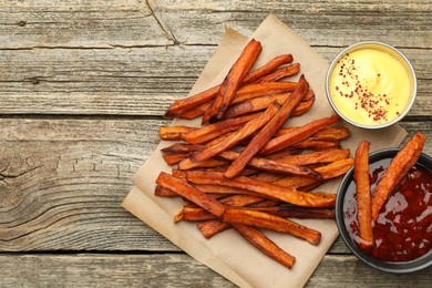 Delicious sweet potato fries with sauces on wooden table, flat lay. Space for text