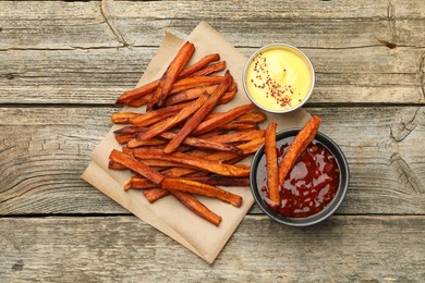 Delicious sweet potato fries with sauces on wooden table, flat lay