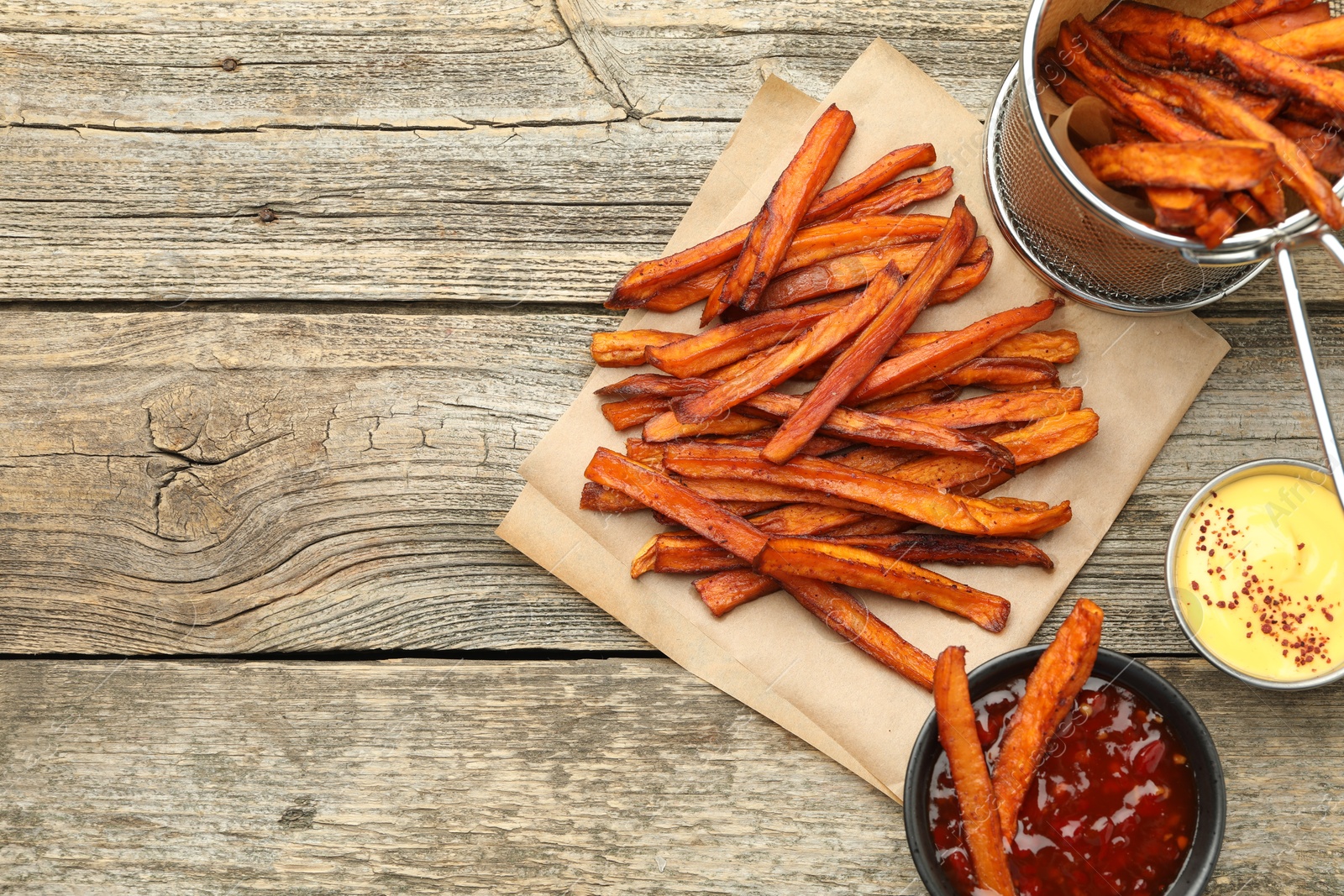 Photo of Delicious sweet potato fries with sauces on wooden table, flat lay. Space for text