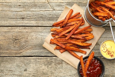 Photo of Delicious sweet potato fries with sauces on wooden table, flat lay. Space for text