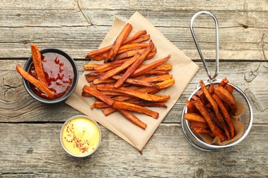 Photo of Delicious sweet potato fries with sauces on wooden table, flat lay