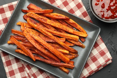 Photo of Delicious sweet potato fries with sauce on black table, top view