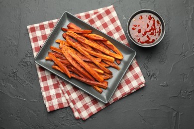 Photo of Delicious sweet potato fries with sauce on black table, top view