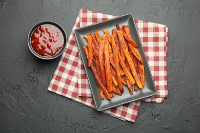 Photo of Delicious sweet potato fries with sauce on black table, top view