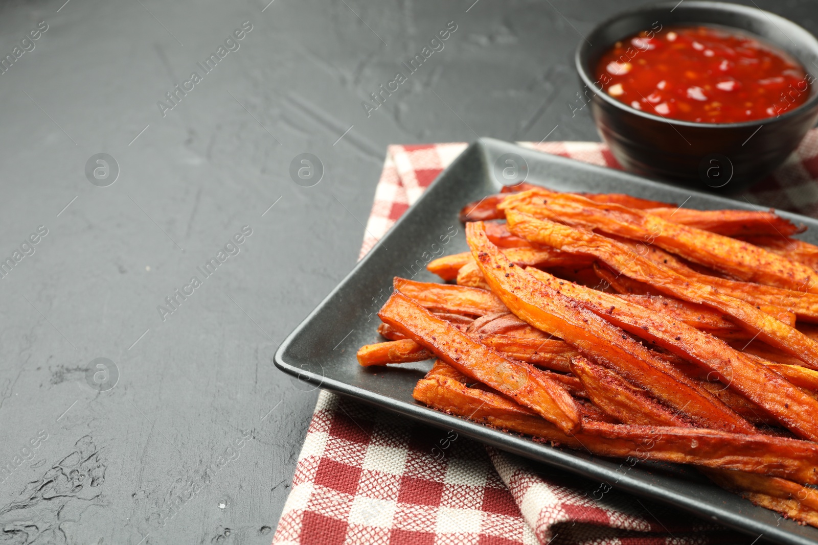 Photo of Delicious sweet potato fries with sauce on black table, closeup. Space for text