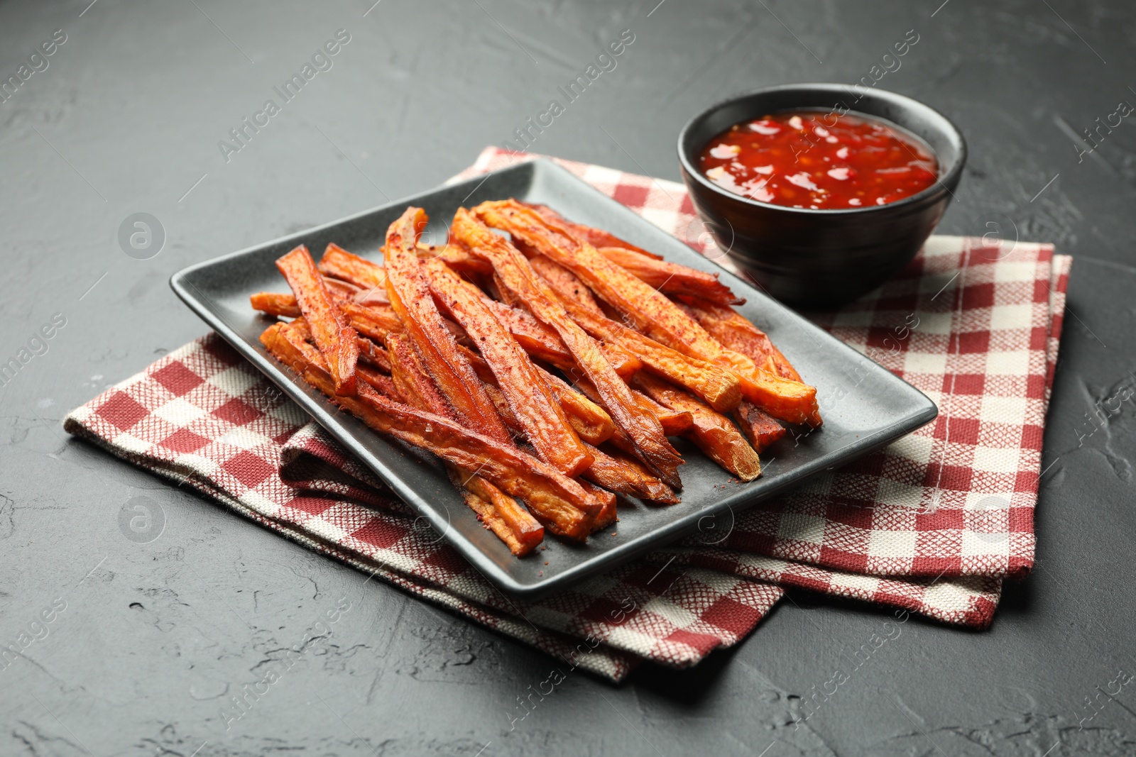 Photo of Delicious sweet potato fries with sauce on black table, closeup