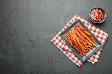 Delicious sweet potato fries with sauce on black table, top view. Space for text