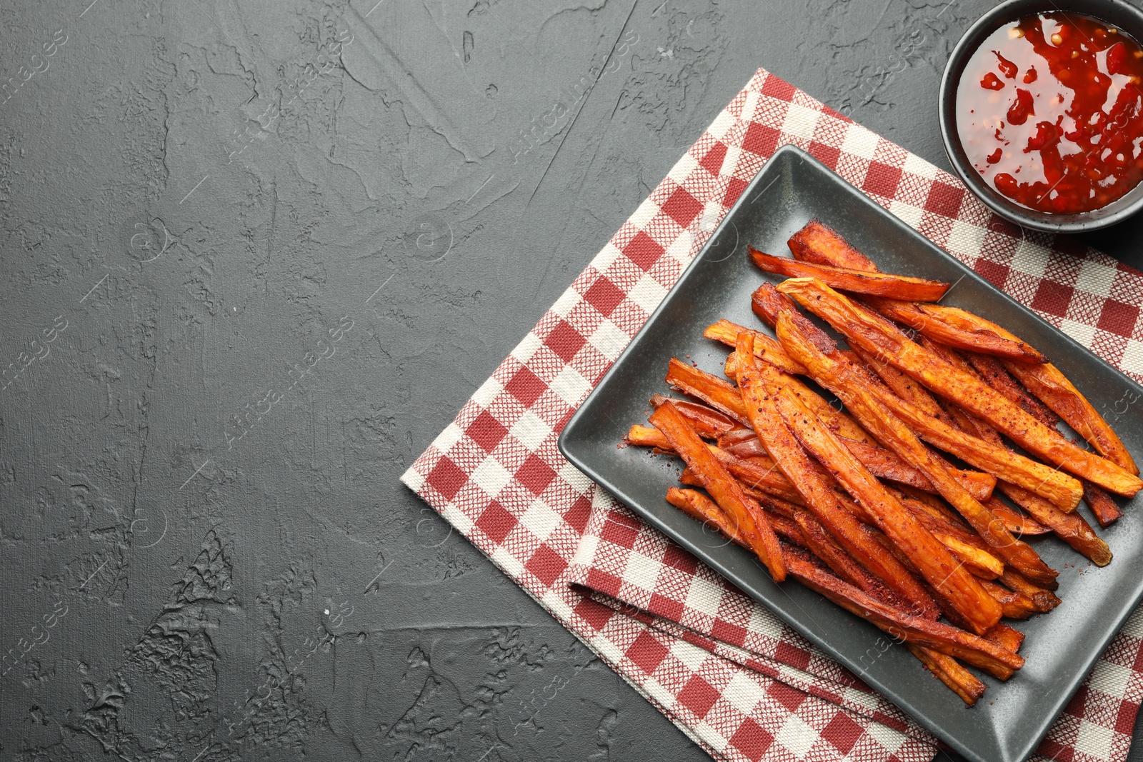 Photo of Delicious sweet potato fries with sauce on black table, top view. Space for text