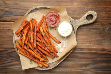 Delicious sweet potato fries with sauces and spices on wooden table, top view