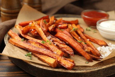 Photo of Delicious sweet potato fries with sauces and spices on wooden table, closeup