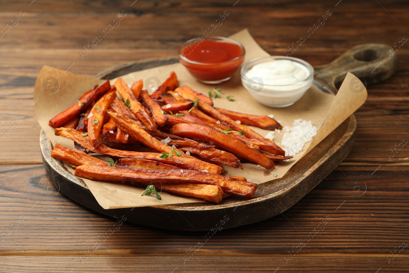 Photo of Delicious sweet potato fries with sauces and spices on wooden table, closeup