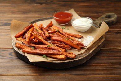 Photo of Delicious sweet potato fries with sauces and spices on wooden table, closeup