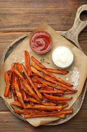 Delicious sweet potato fries with sauces and spices on wooden table, top view