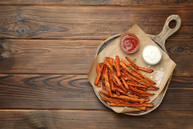 Photo of Delicious sweet potato fries with sauces and spices on wooden table, top view. Space for text