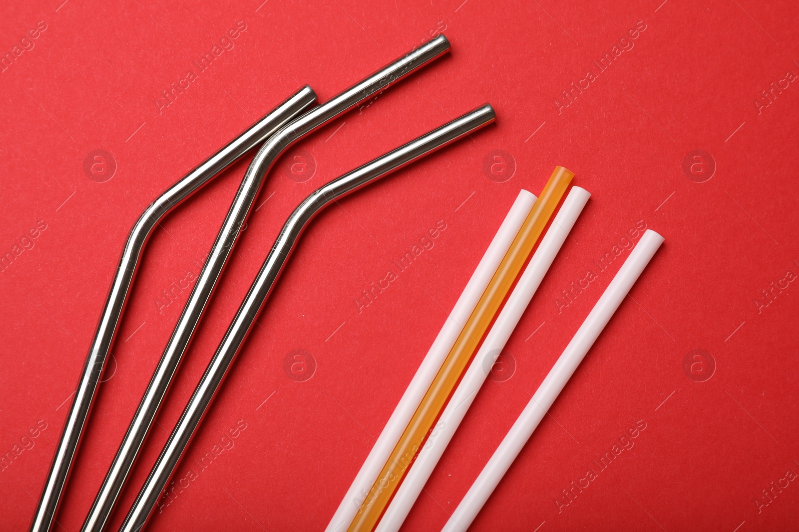 Photo of Plastic and metal drinking straws on red background, top view