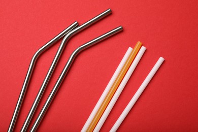 Photo of Plastic and metal drinking straws on red background, top view