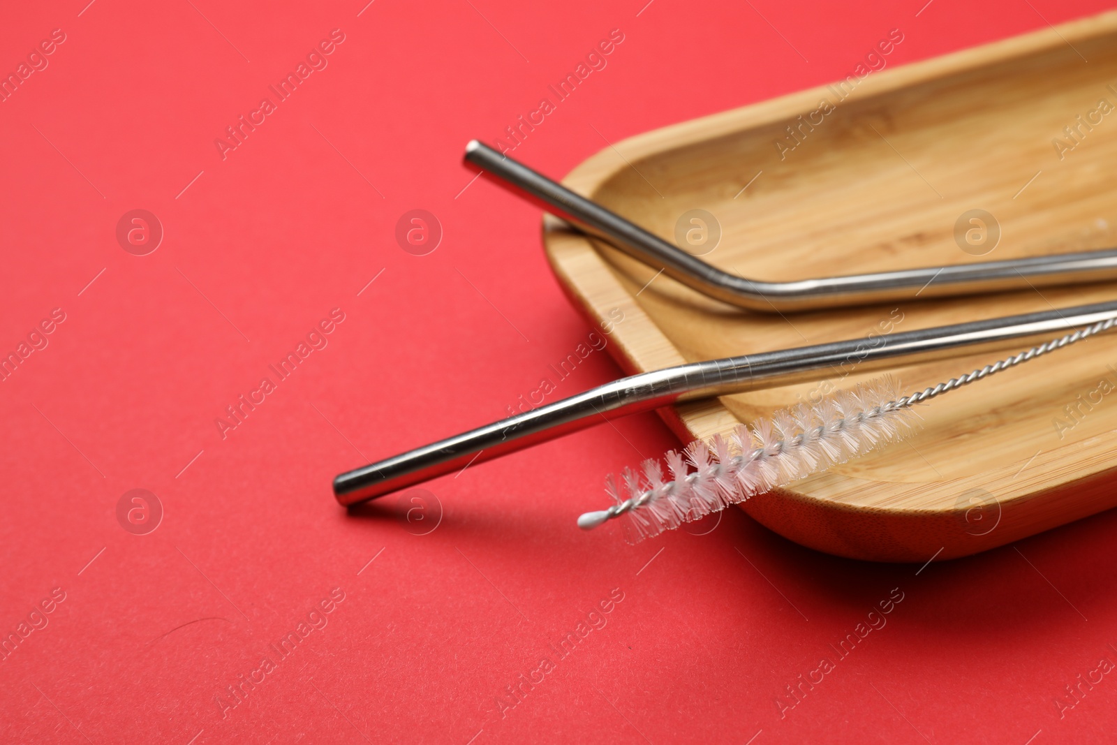 Photo of Metal drinking straws and cleaning brush on red background, closeup. Space for text