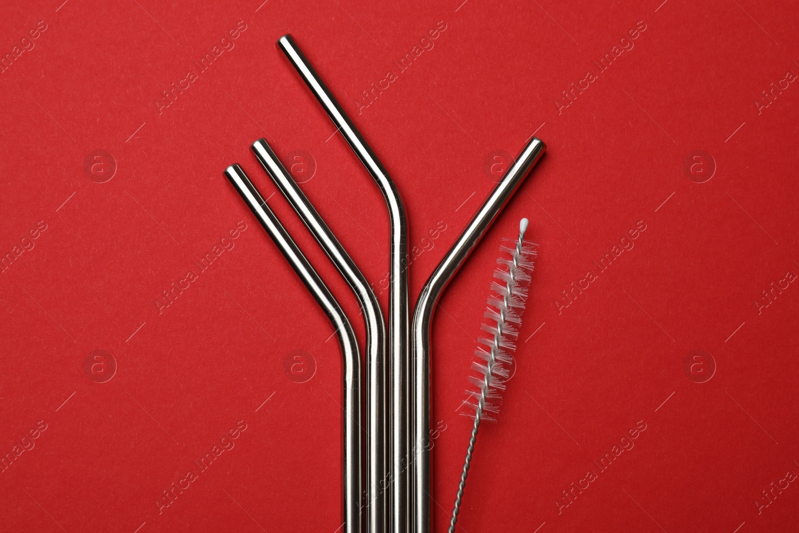 Photo of Metal drinking straws and cleaning brush on red background, top view