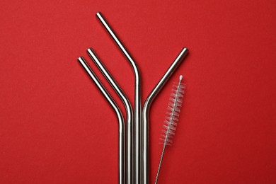 Photo of Metal drinking straws and cleaning brush on red background, top view