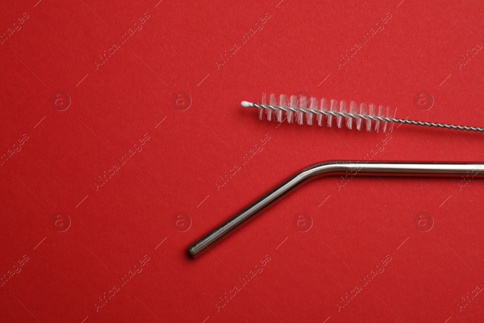 Photo of Metal drinking straw and cleaning brush on red background, top view