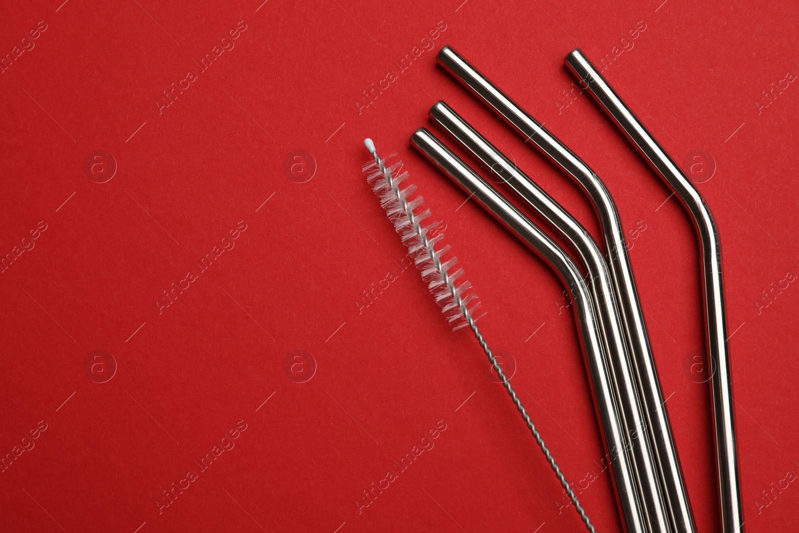 Photo of Metal drinking straws and cleaning brush on red background, top view. Space for text