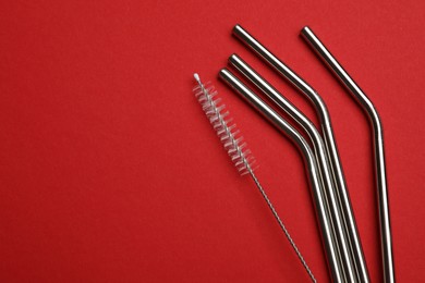 Photo of Metal drinking straws and cleaning brush on red background, top view. Space for text