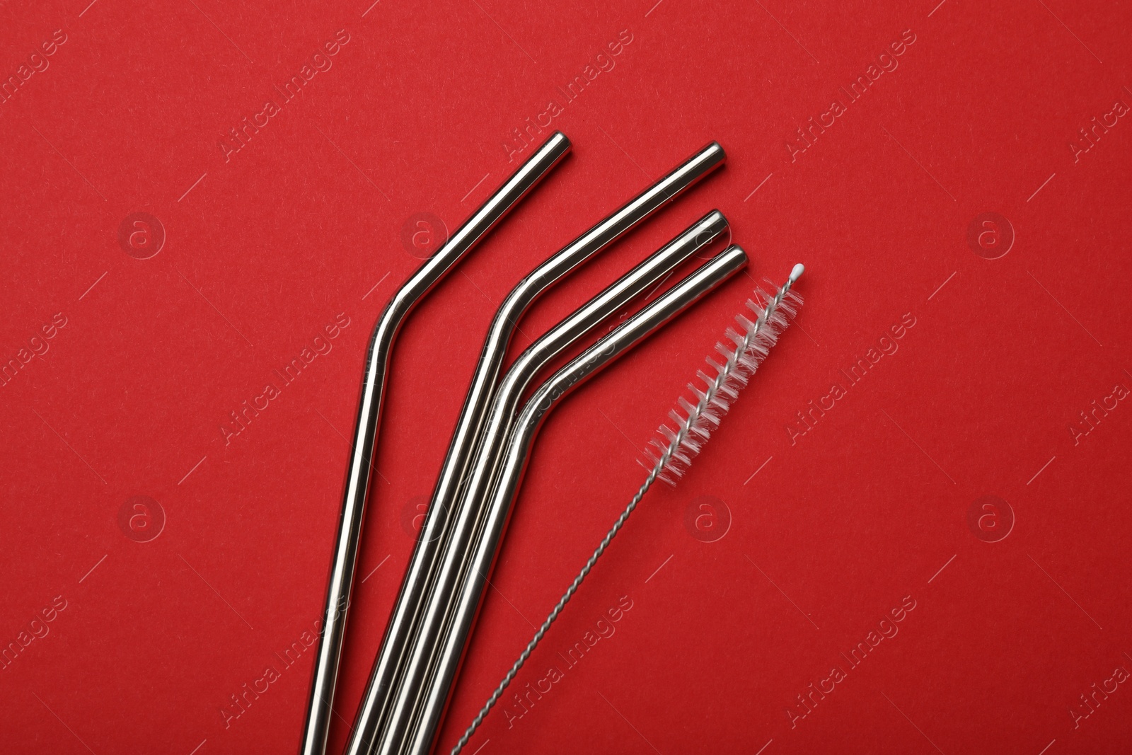 Photo of Metal drinking straws and cleaning brush on red background, top view