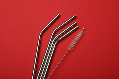 Photo of Metal drinking straws and cleaning brush on red background, top view