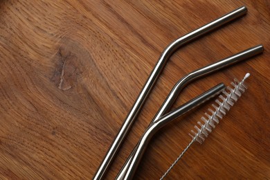 Photo of Metal drinking straws and cleaning brush on wooden background, top view. Space for text