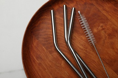 Photo of Metal drinking straws and cleaning brush on wooden tray, top view