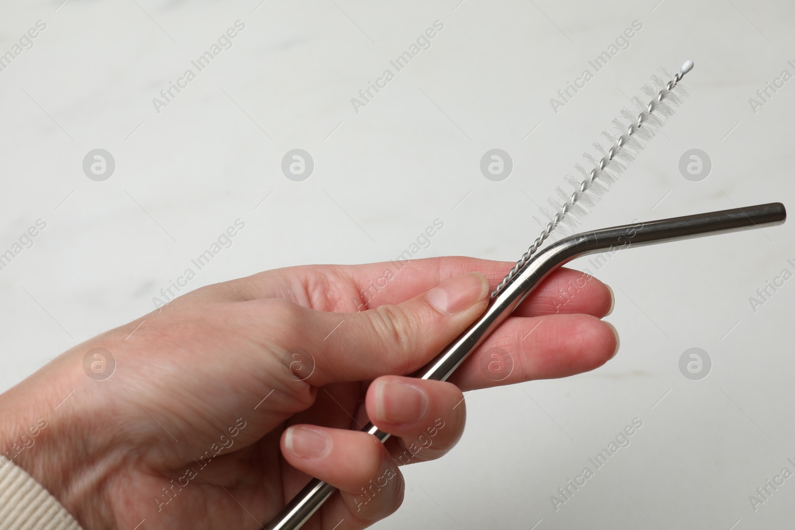 Photo of Woman holding metal drinking straw and cleaning brush on light background, closeup