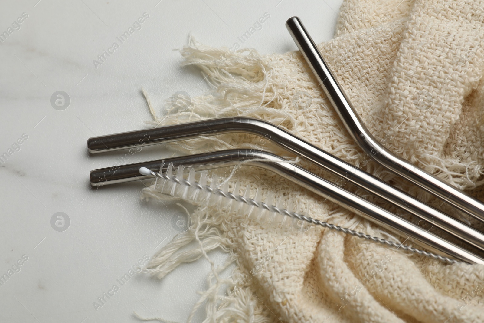 Photo of Metal drinking straws and cleaning brush on marble table, closeup