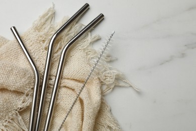 Photo of Metal drinking straws and cleaning brush on marble table, top view. Space for text