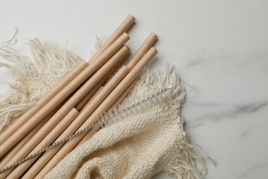 Photo of Bamboo drinking straws and cleaning brush on marble table, top view