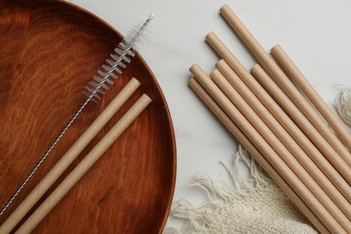 Photo of Bamboo drinking straws and cleaning brush on marble table, top view